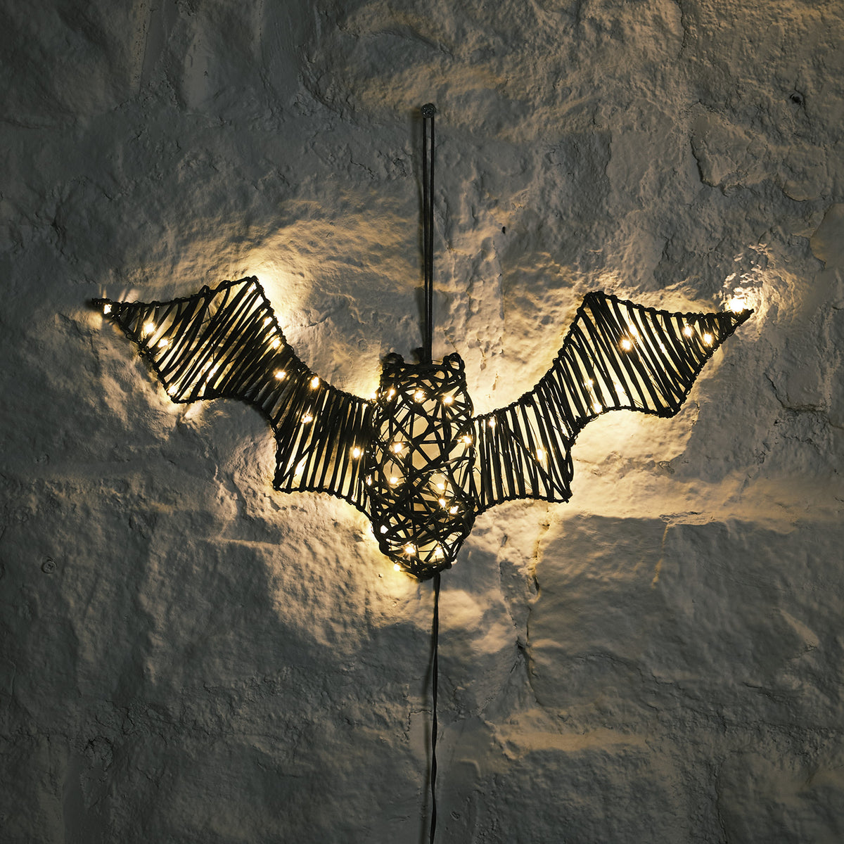 LED Fledermaus aus Rattan-Optik mit warmweißen Lichtern an einer rauen Wand