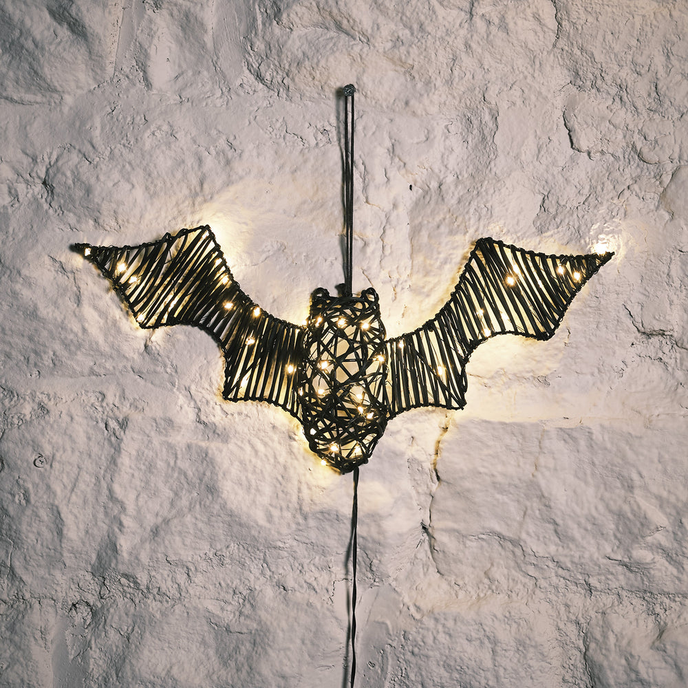 Beleuchtete Rattan-Fledermaus mit warmweißen LEDs vor heller Wand hängend