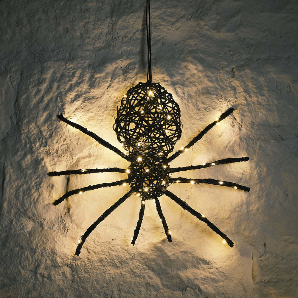 Beleuchtete Rattan Spinne mit warmweißen LEDs an weißer Wand im Dunkeln