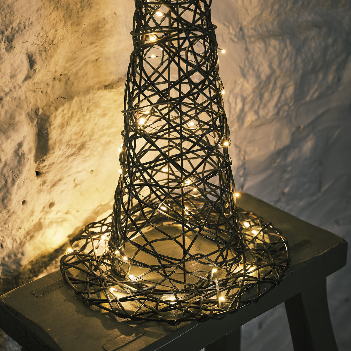 Nahaufnahme des beleuchteten Rattan Hexenhuts mit warmweißen LEDs auf grauem Hocker