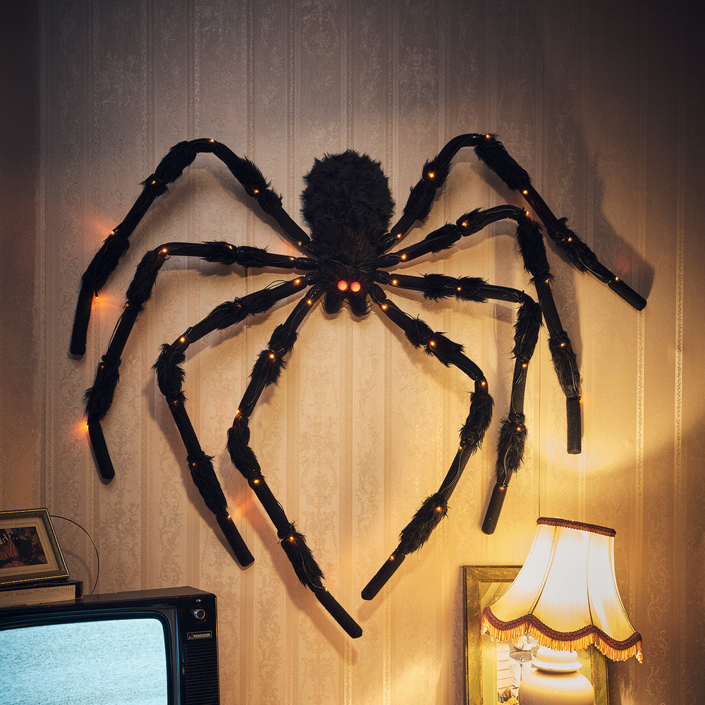 LED-Spinnenfigur mit roten Augen und orangefarbenen Lichtern an einer Tapetenwand neben Lampe und Fernseher