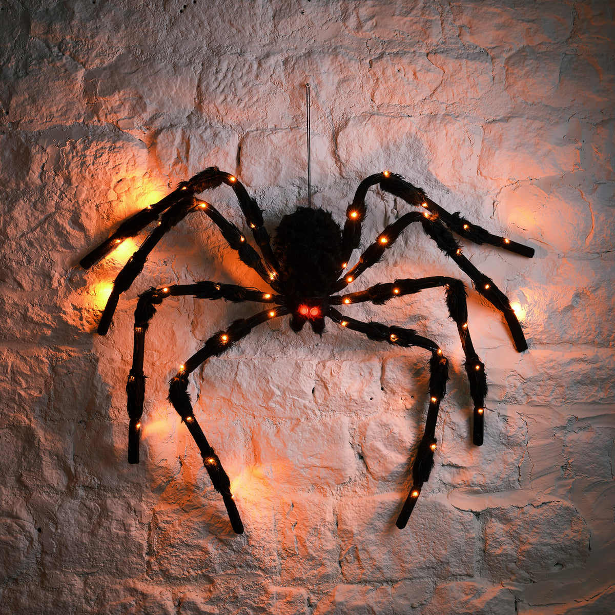 Große schwarze LED-Spinnenfigur mit orangefarbenen Lichtern an einer weißen Steinwand