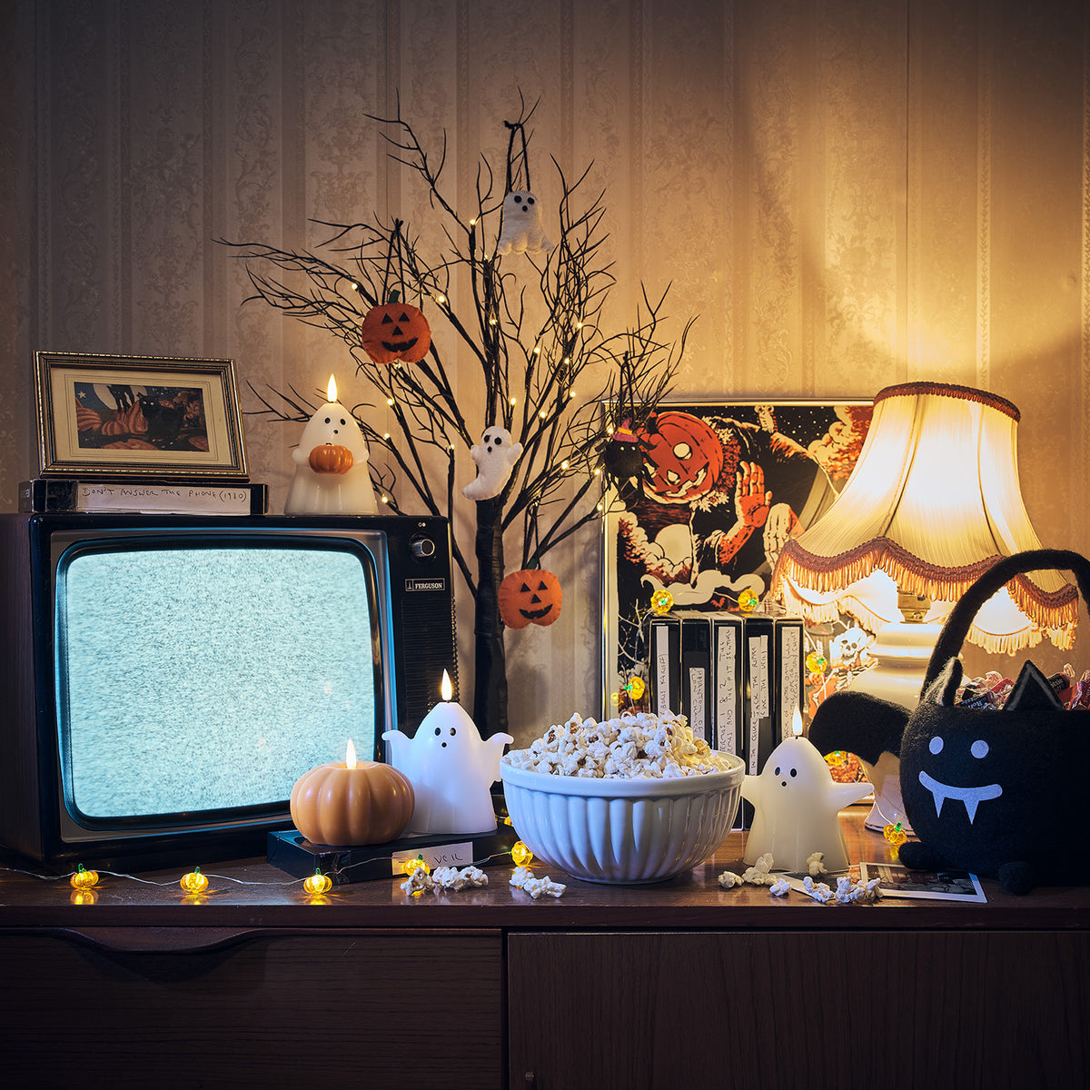 Beleuchteter schwarzer Halloween-Dekobaum mit Mini-Kürbissen und Geisteranhängern neben Fernseher