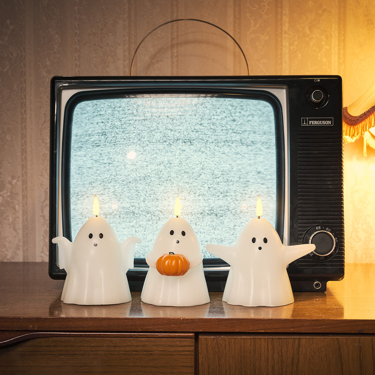 Drei leuchtende Geister-LED-Kerzen vor einem alten Fernseher mit Schneebildschirm auf einem Holztisch