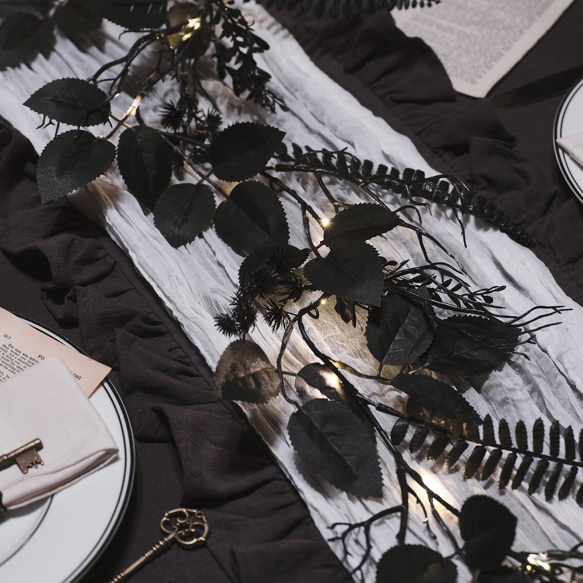 Schwarze Halloween-Girlande mit Blättern und warmweißen LEDs auf weißem Stoff auf dunklem Untergrund