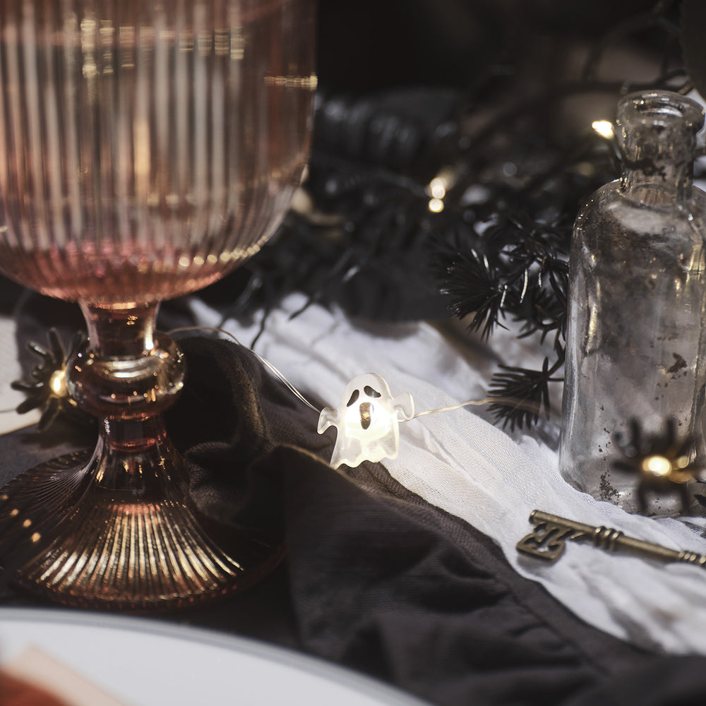 Halloween-Geist leuchtet neben rosa Glas und schwarzem Stoff auf gedecktem Tisch