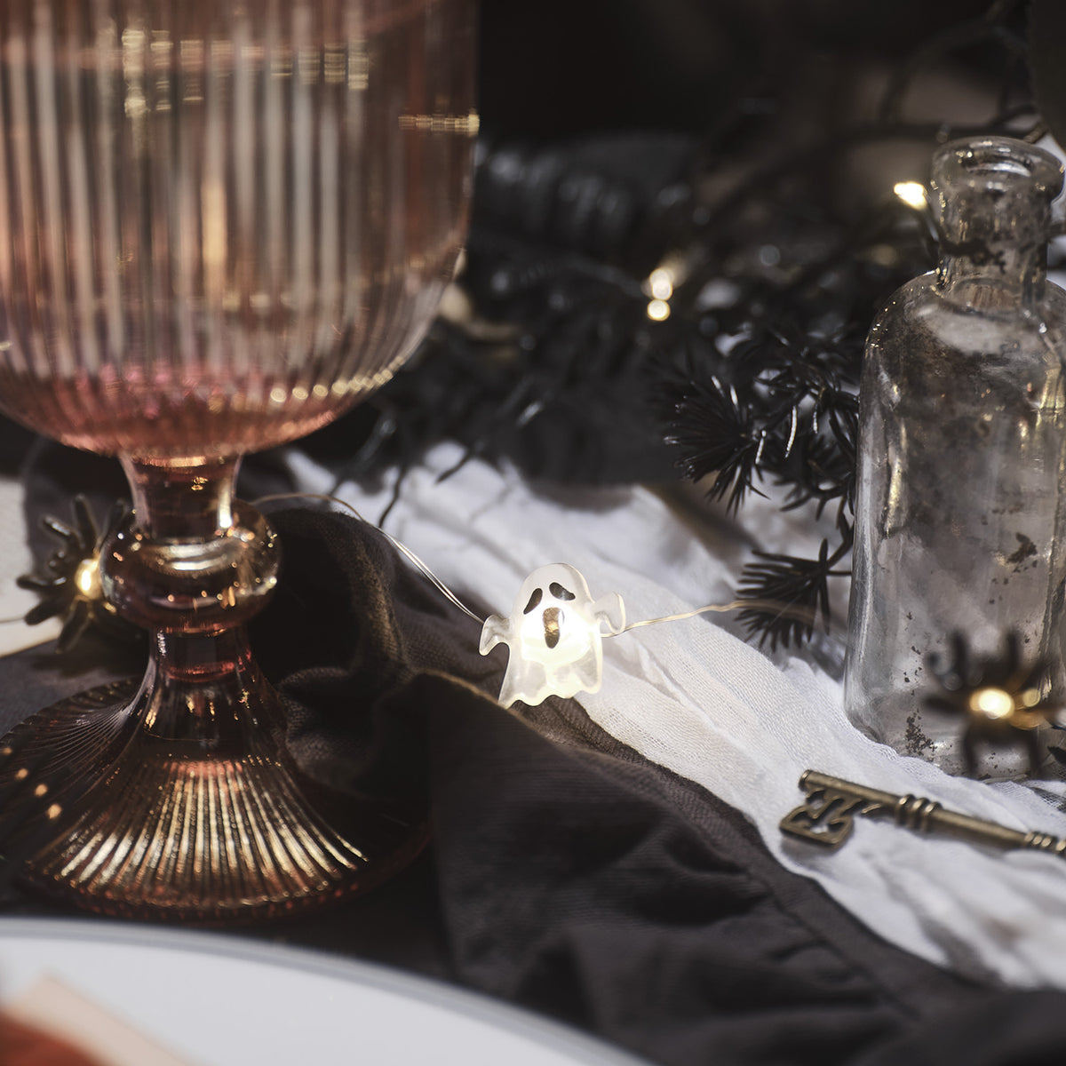 Halloween-Geist leuchtet neben rosa Glas und schwarzem Stoff auf gedecktem Tisch