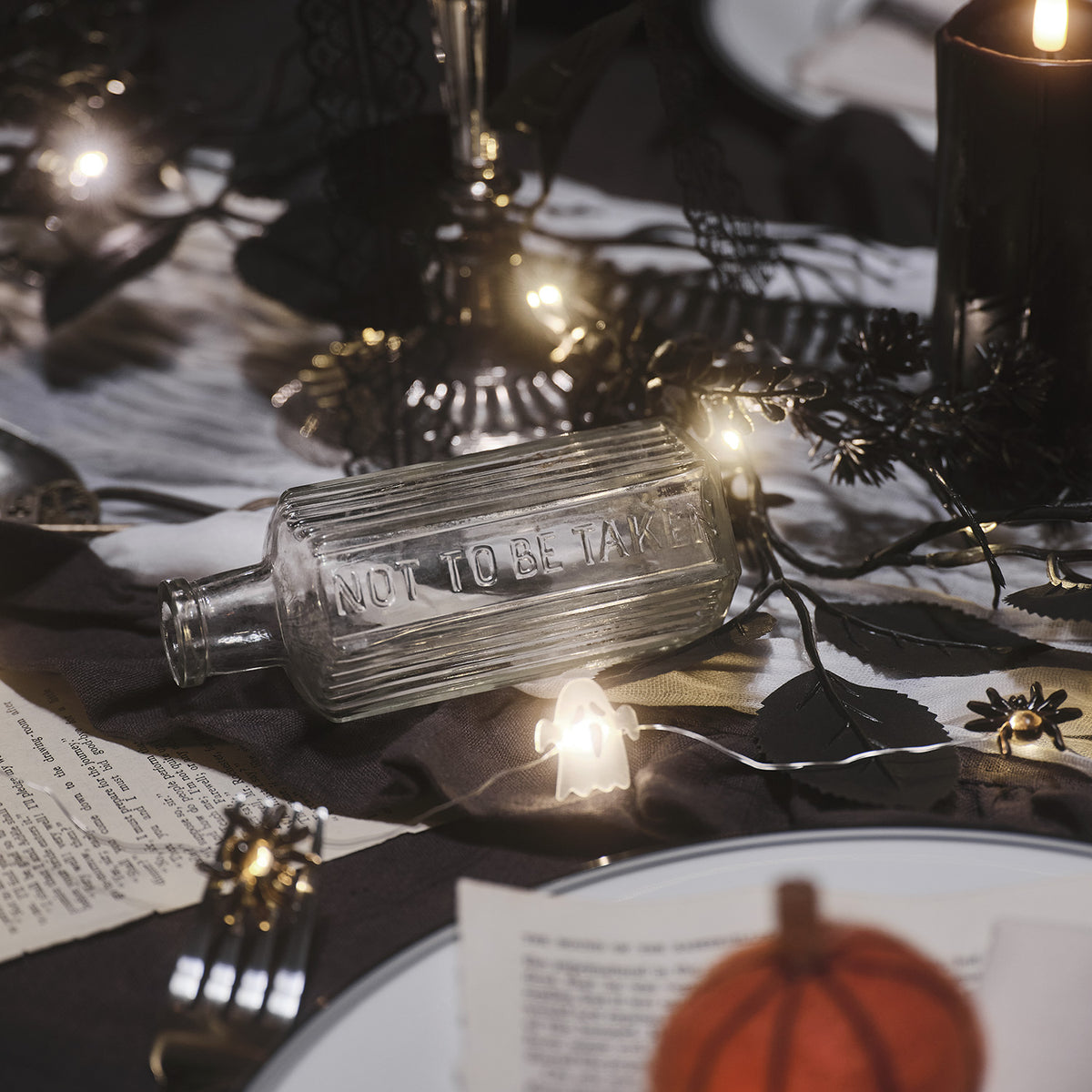 Halloween-Lichterkette mit Geistern und Spinnen um eine Glasflasche auf dunklem Stoff