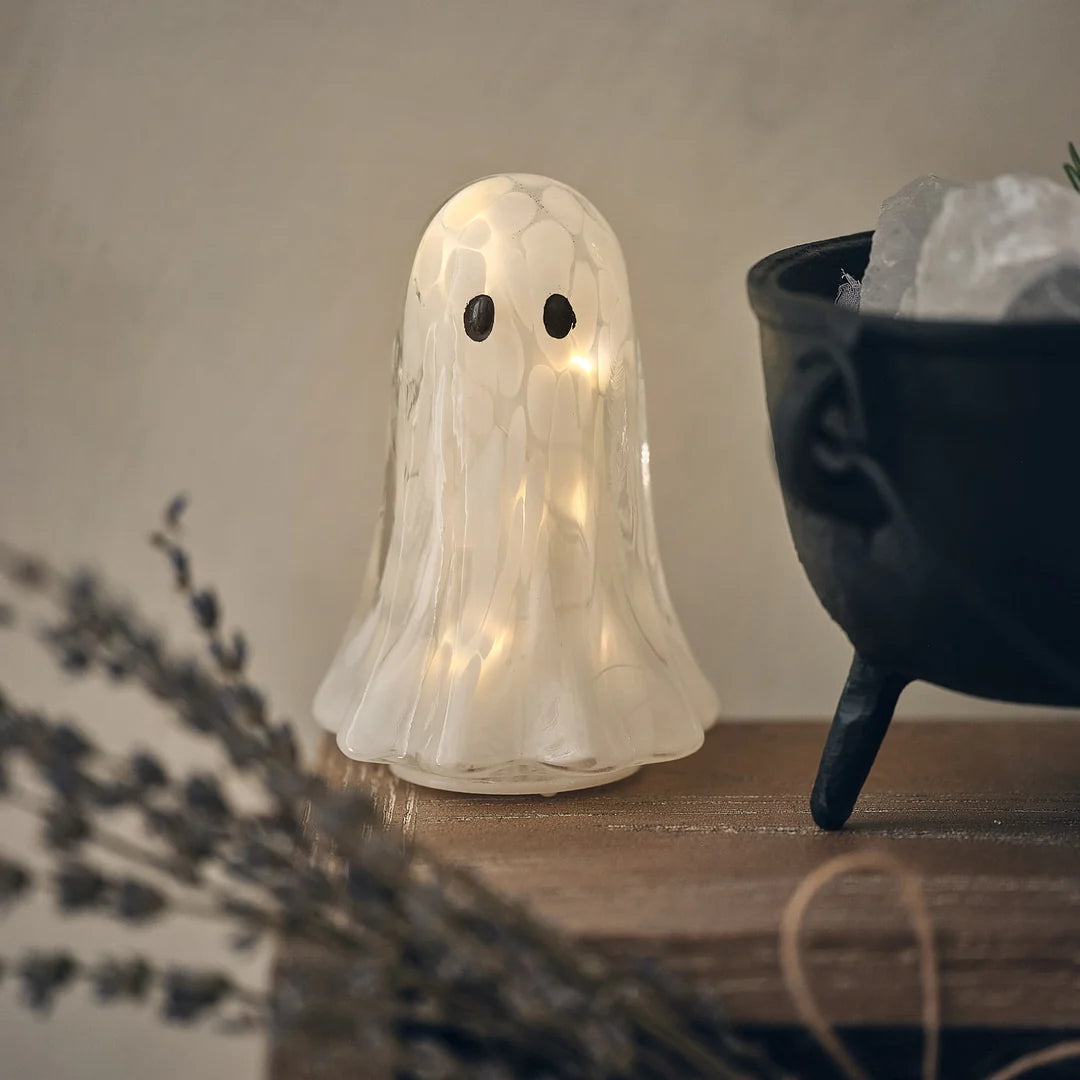 LED-Halloween-Geist aus Konfettiglas vor schwarzem Kessel und getrockneten Zweigen