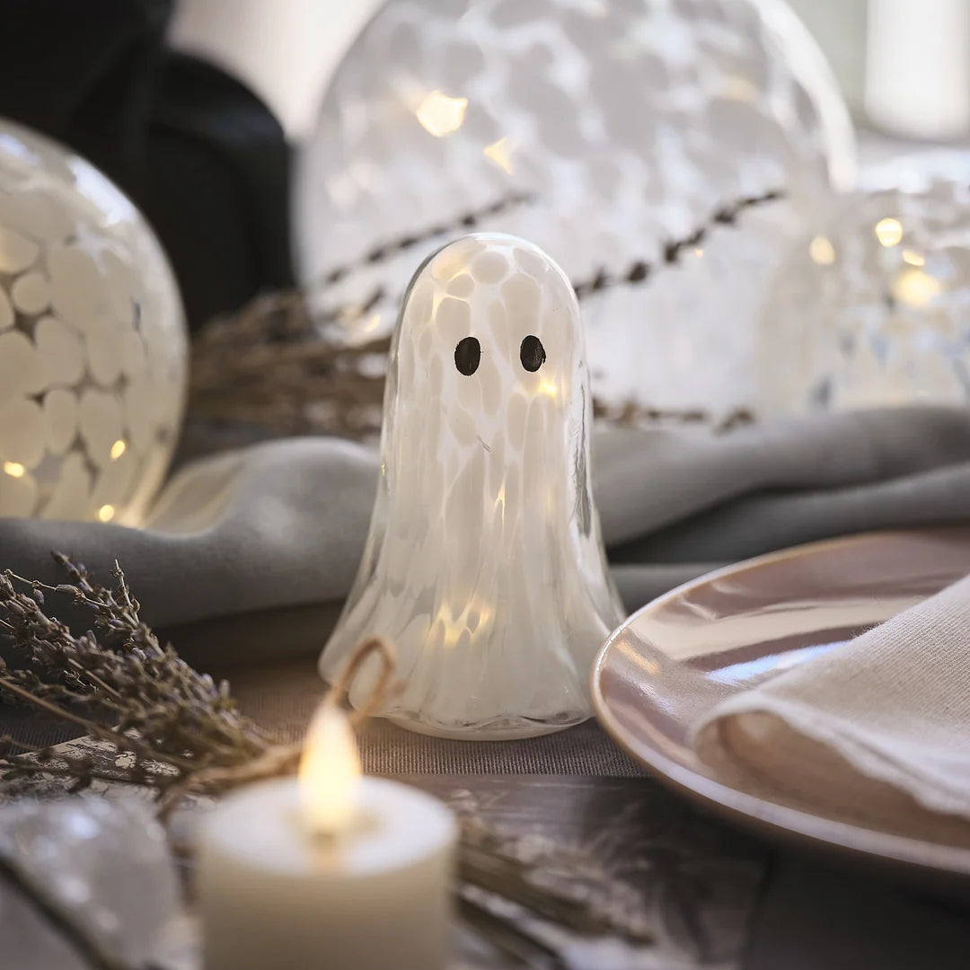 Kleine LED-Halloween-Geist-Deko aus Konfettiglas neben Kerze und Teller auf Tisch