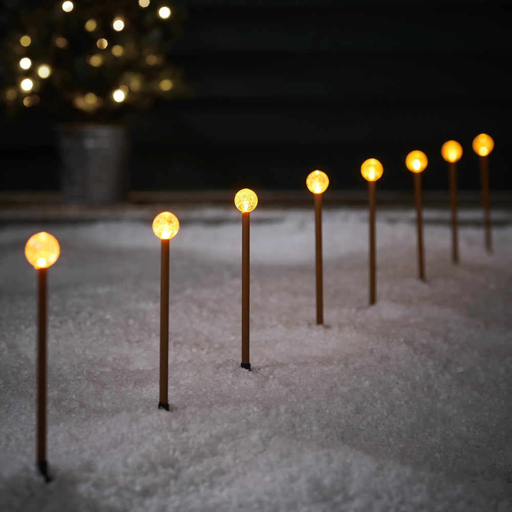 Acht LED Stableuchten mit klaren Kugeln auf rostfarbenen Stäben im Schnee bei Nacht