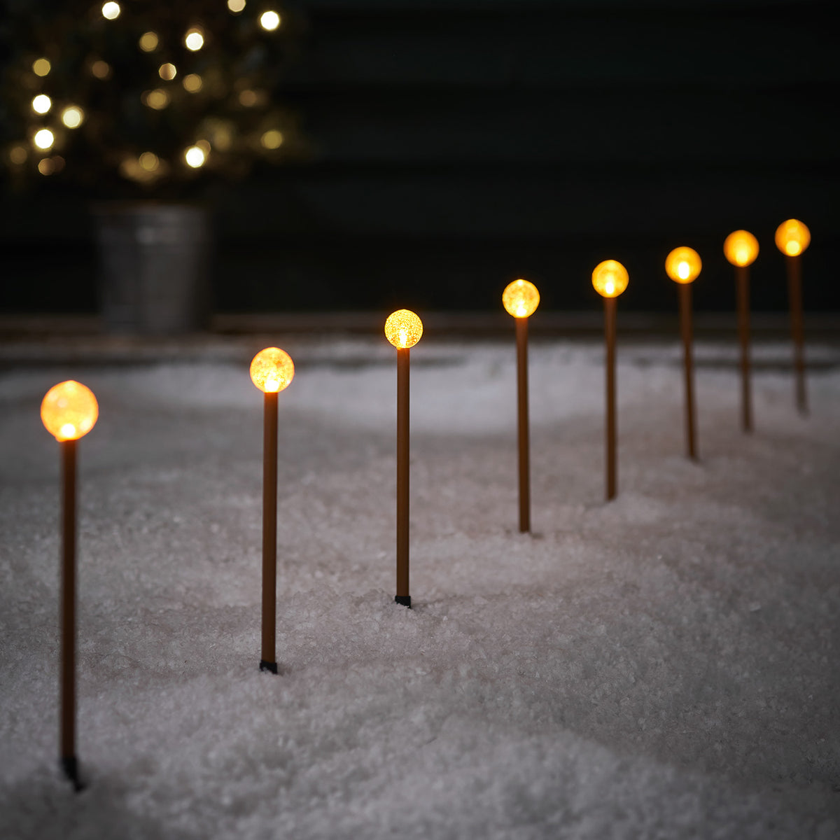 Acht LED Stableuchten mit klaren Kugeln auf rostfarbenen Stäben im Schnee bei Nacht
