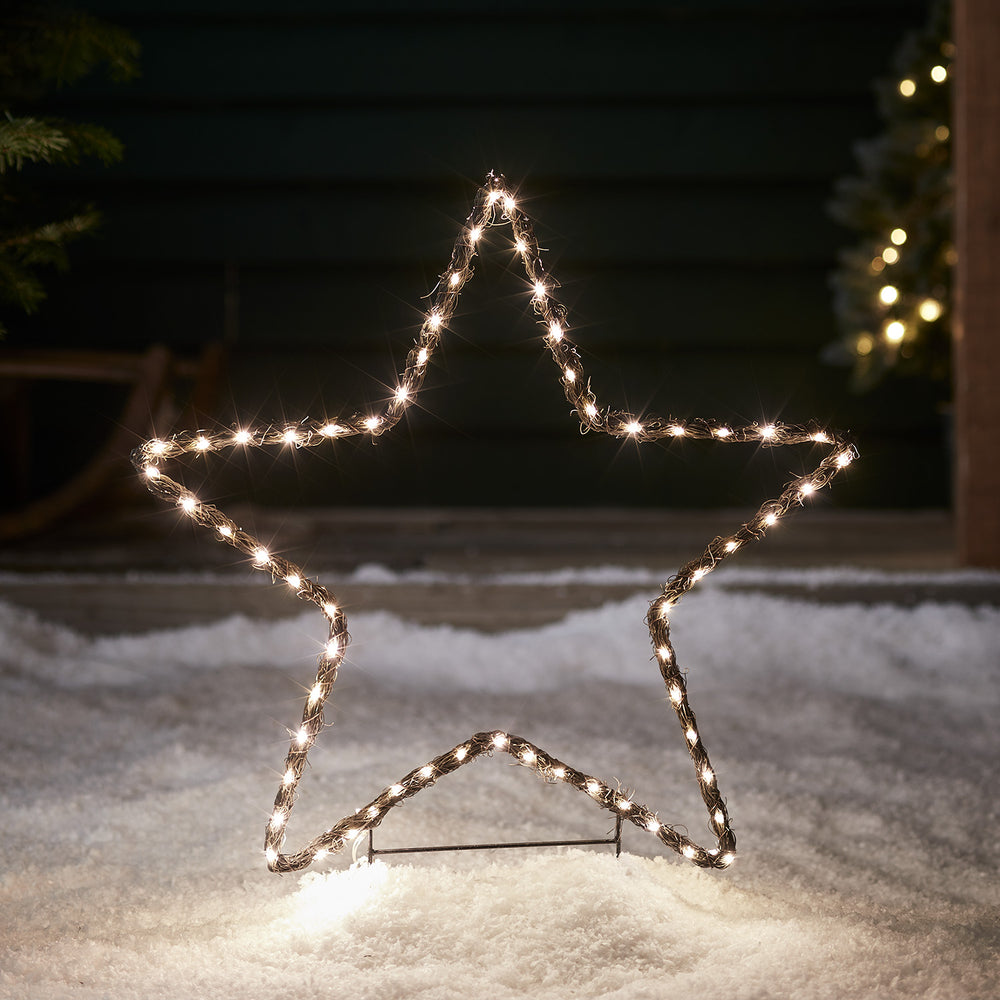 Leuchtender Stern aus Weide mit warmweißen LEDs im Schnee bei Nacht