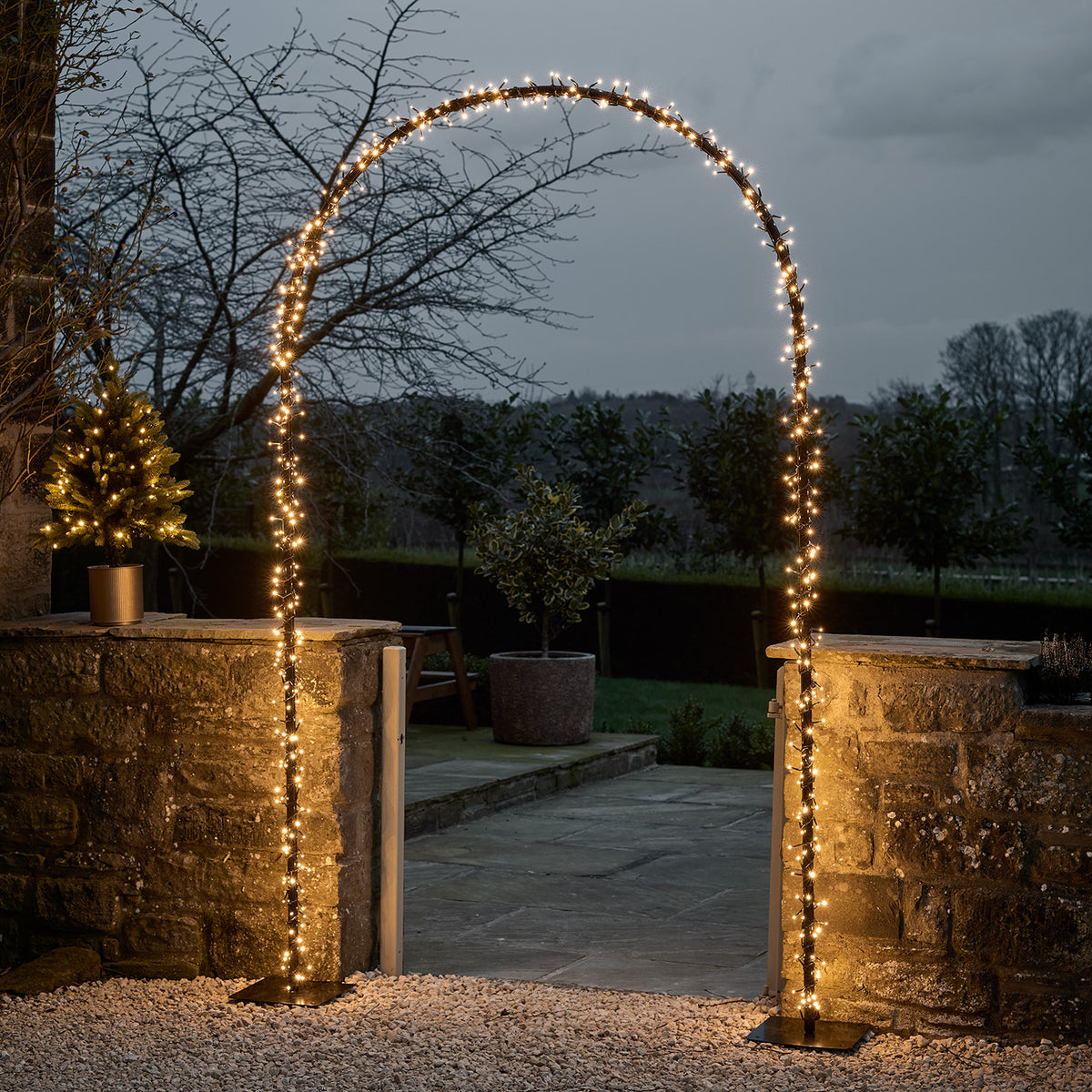 LED Torbogen mit warmweißen Lichtern beleuchtet einen Gartenweg bei Dämmerung