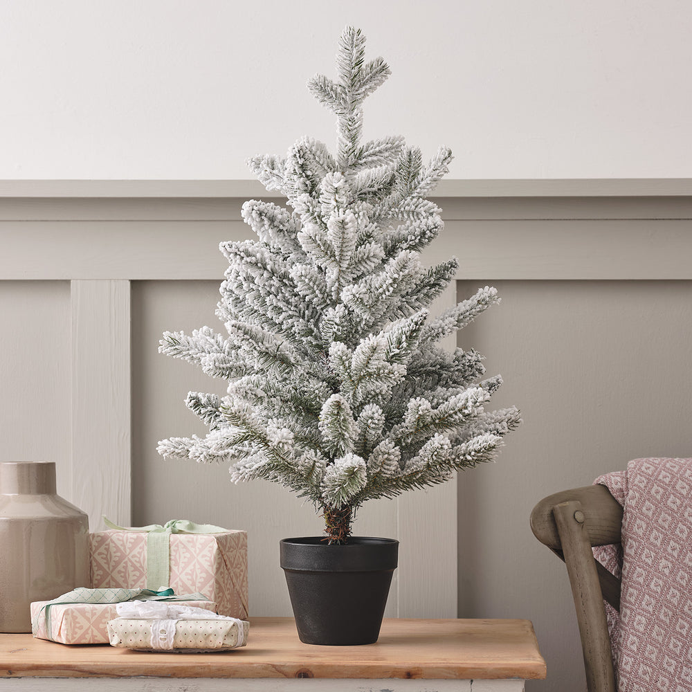 60 cm großer künstlicher Weihnachtsbaum mit Schnee-Effekt in schwarzem Topf auf Holztisch