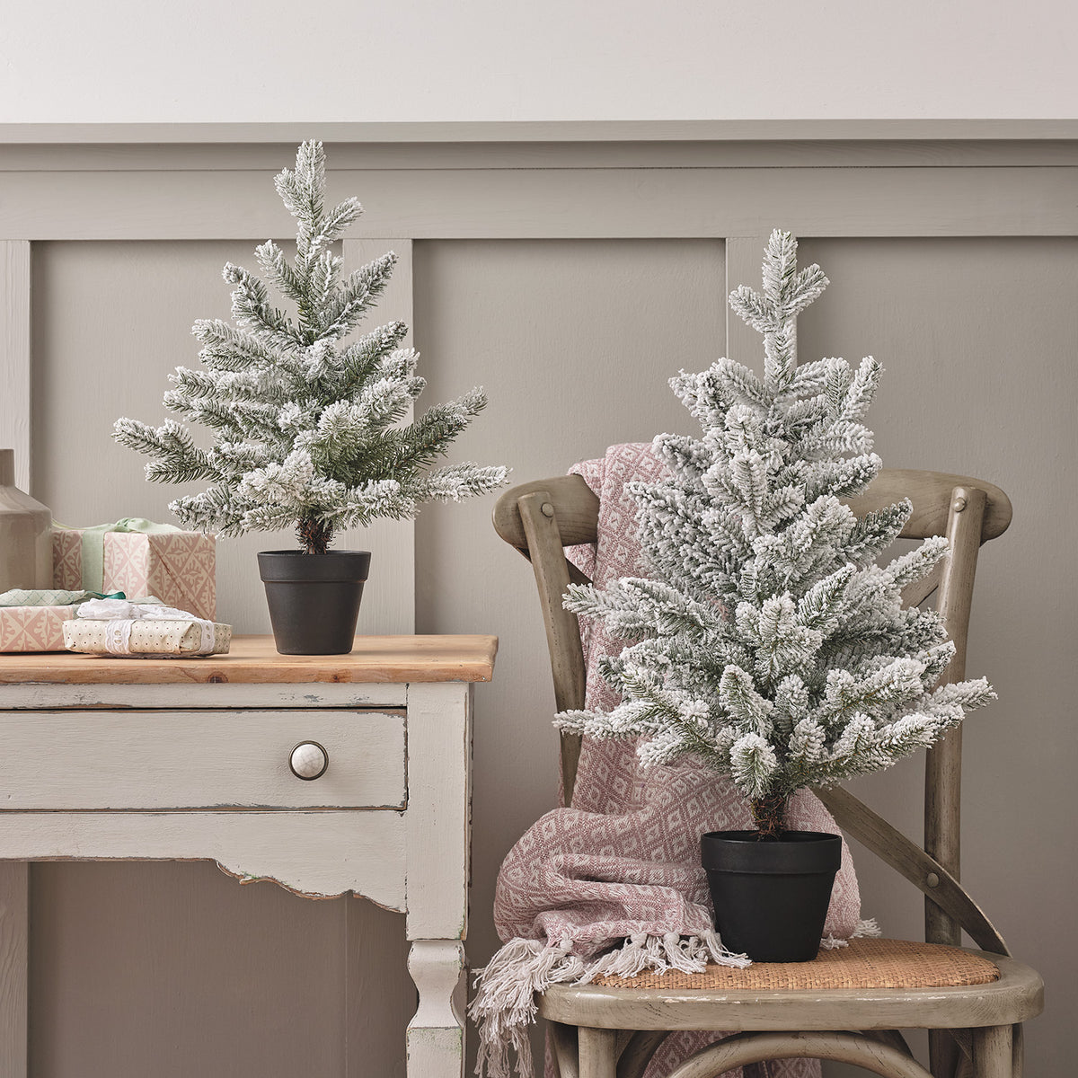 Zwei verschneite Mini-Weihnachtsbäume auf Stuhl und Kommode mit rosa Decke
