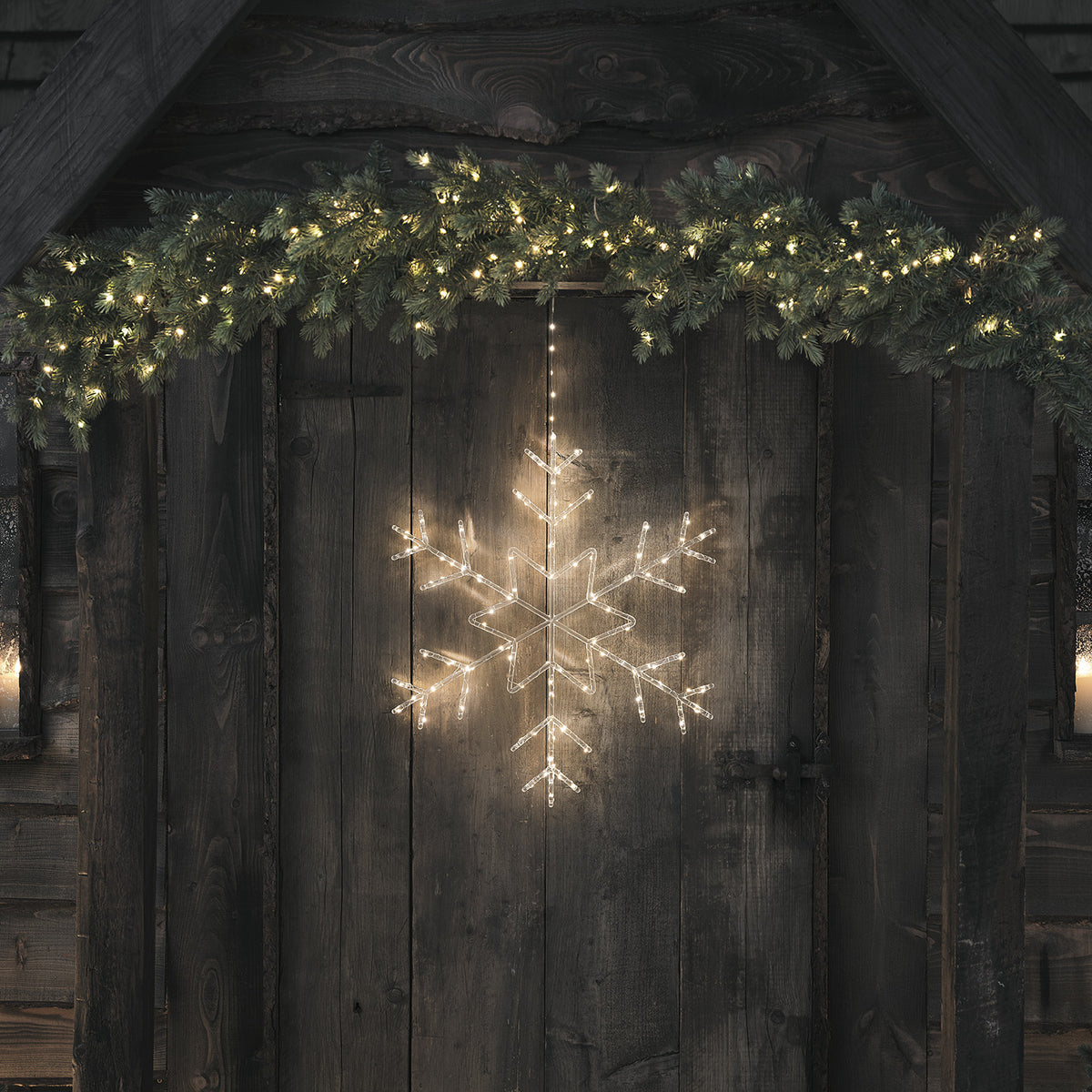 LED-Schneeflocke aus Acryl hängt unter Tannengirlande an Holztür