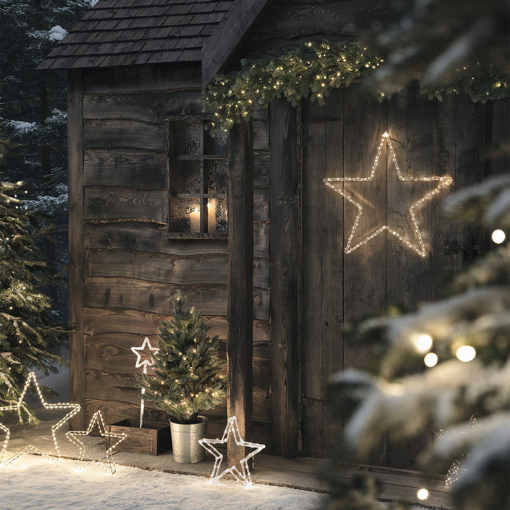 Weihnachtliche Dekoration mit leuchtendem Stern an Holzhütte und Tannenzweigen