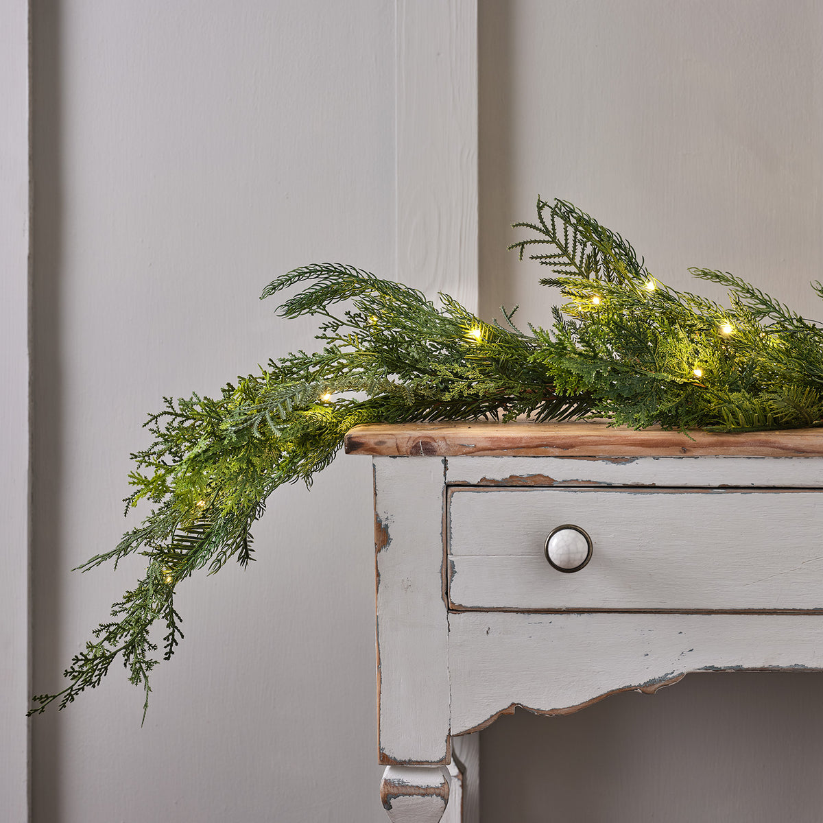 Künstliche Zypressen-Girlande mit eingeschalteter Micro LED Lichterkette auf einem weißen Holztisch