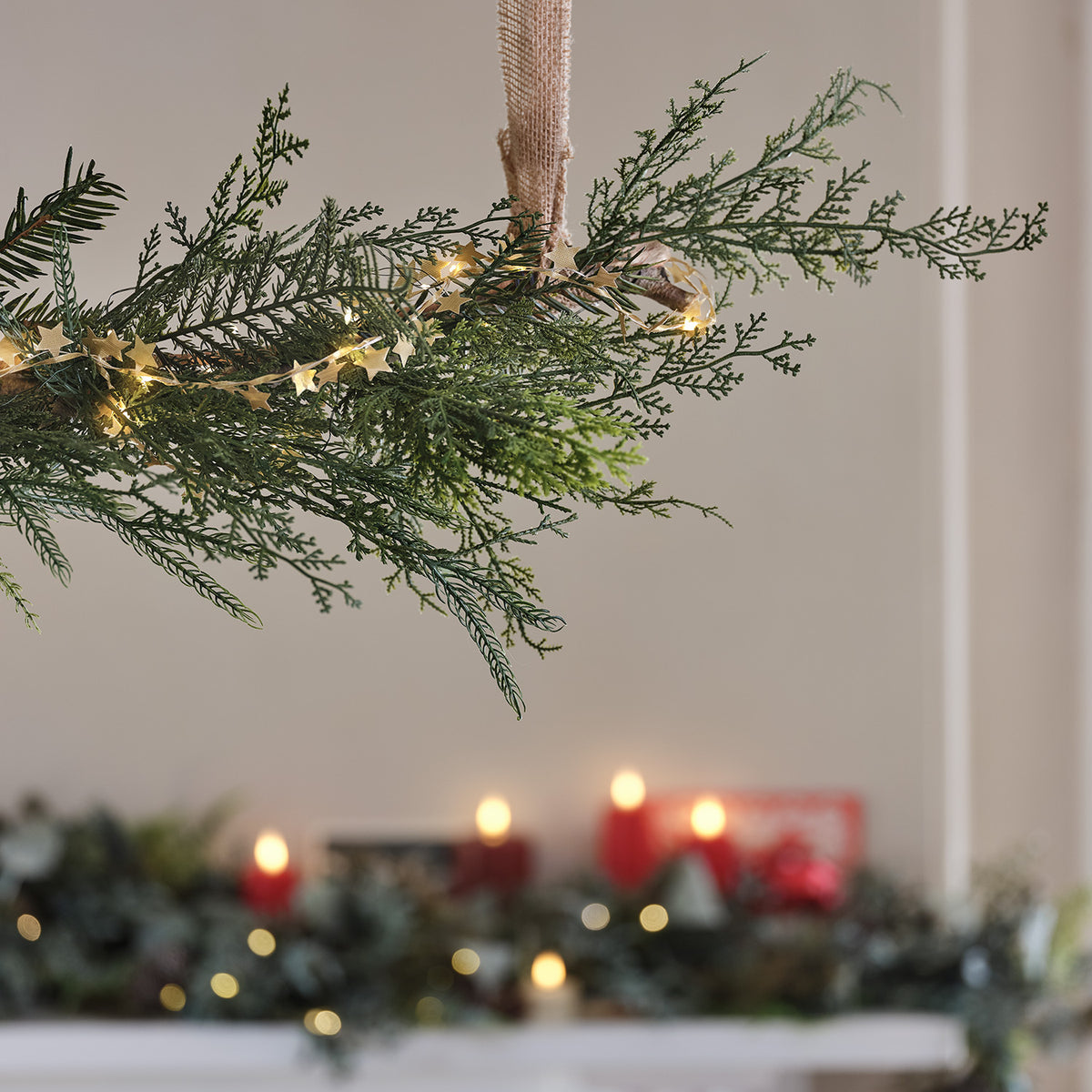 Nahaufnahme einer künstlichen Zypressen-Weihnachtsgirlande mit Sternen-Lichterkette vor Kerzenlicht