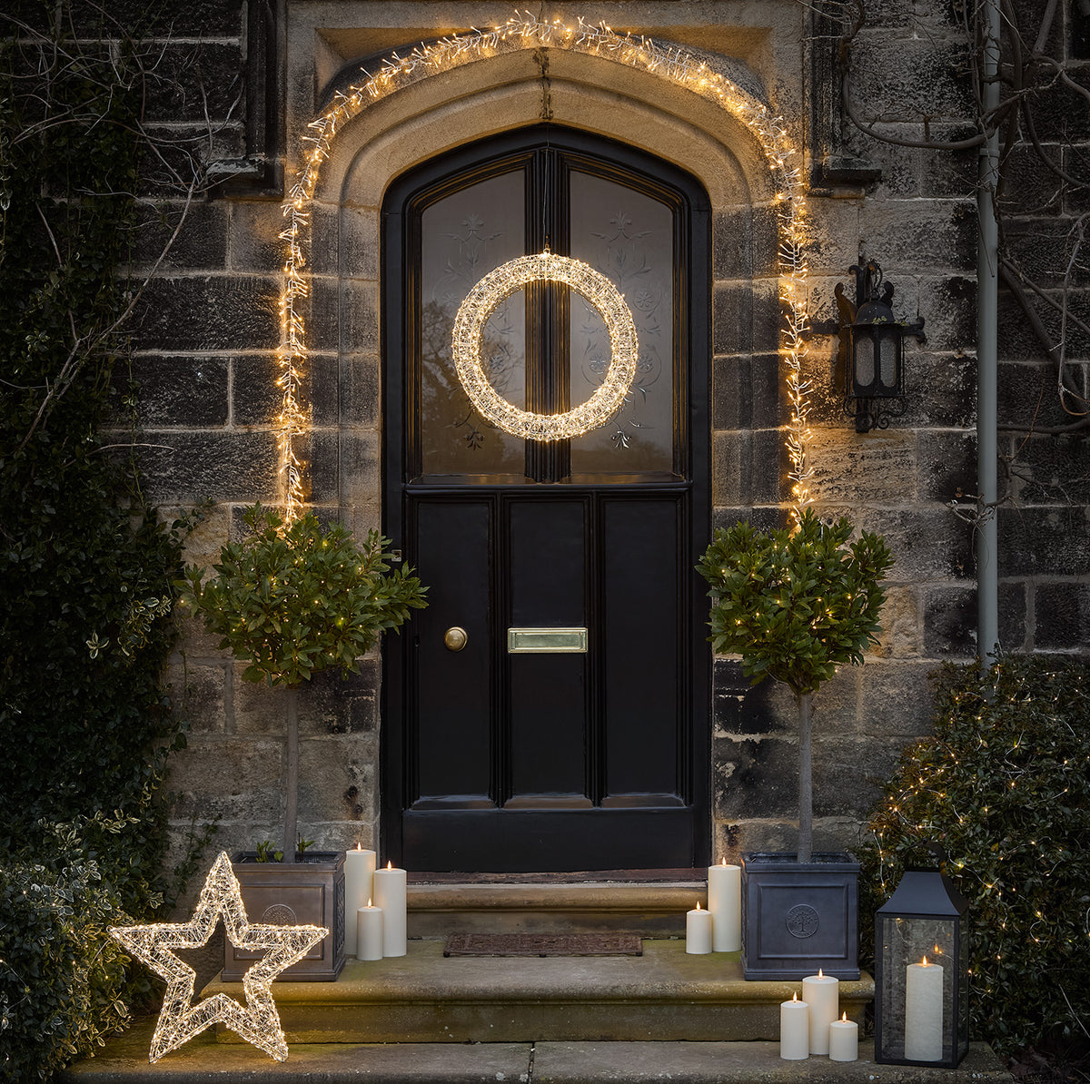 Weihnachtliche Haustür mit beleuchtetem Kranz, LED-Stern und Kerzen auf der Treppe