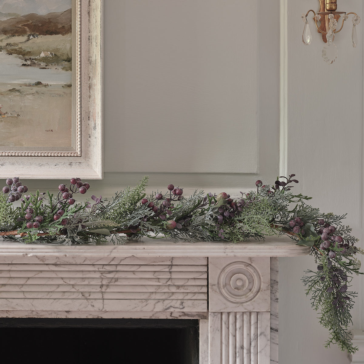 Winterliche Girlande mit violetten Beeren und warmweißen LED-Lichtern auf Kaminsims