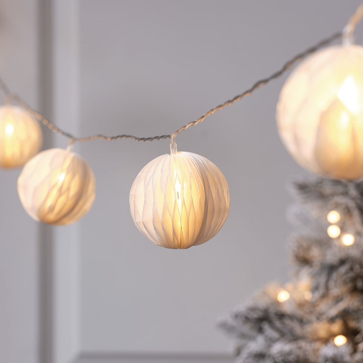 Nahaufnahme einer beleuchteten Papierkugel der LED-Lampion-Lichterkette vor grauer Wand