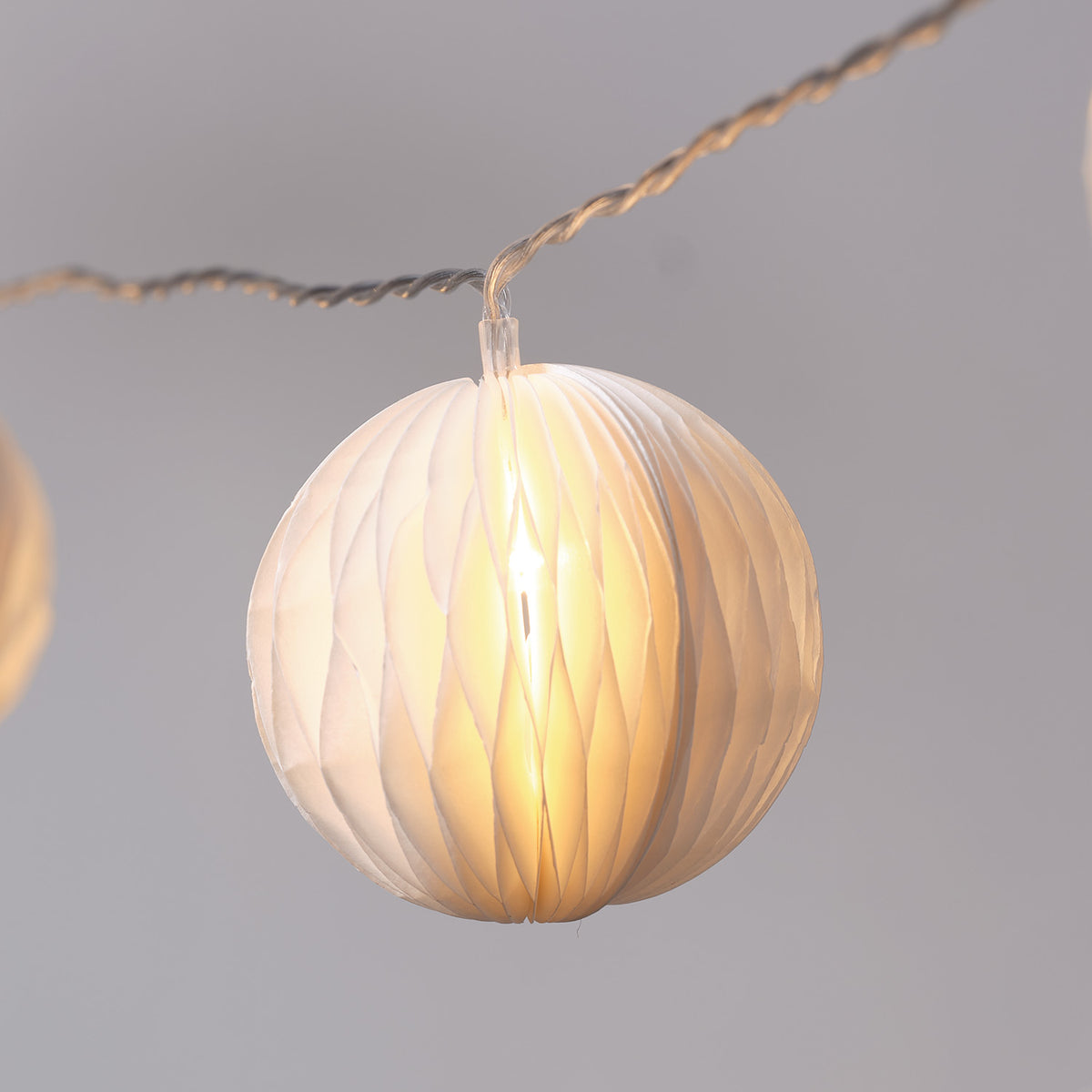 Detailansicht einer cremefarbenen Papierkugel mit warmweißem LED-Licht im Inneren