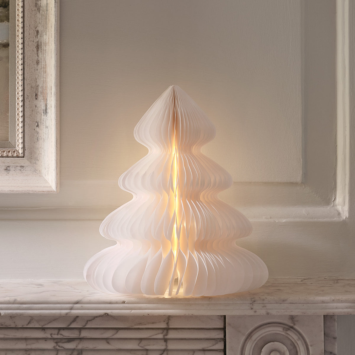 Weißer Origami-Weihnachtsbaum aus Papier mit warmweißer LED-Beleuchtung auf Fensterbank