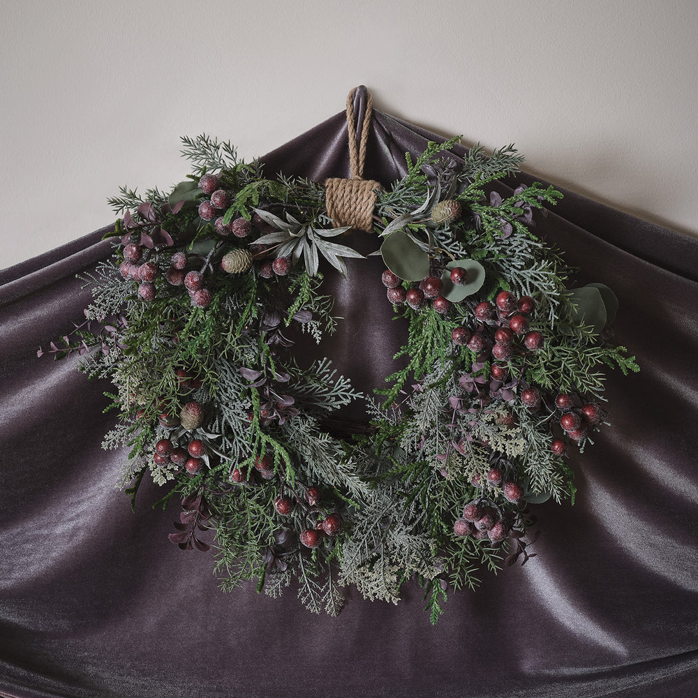 Nahaufnahme des Weihnachtskranzes mit lila Beeren, grünen Zweigen und warmweißen LED-Lichtern