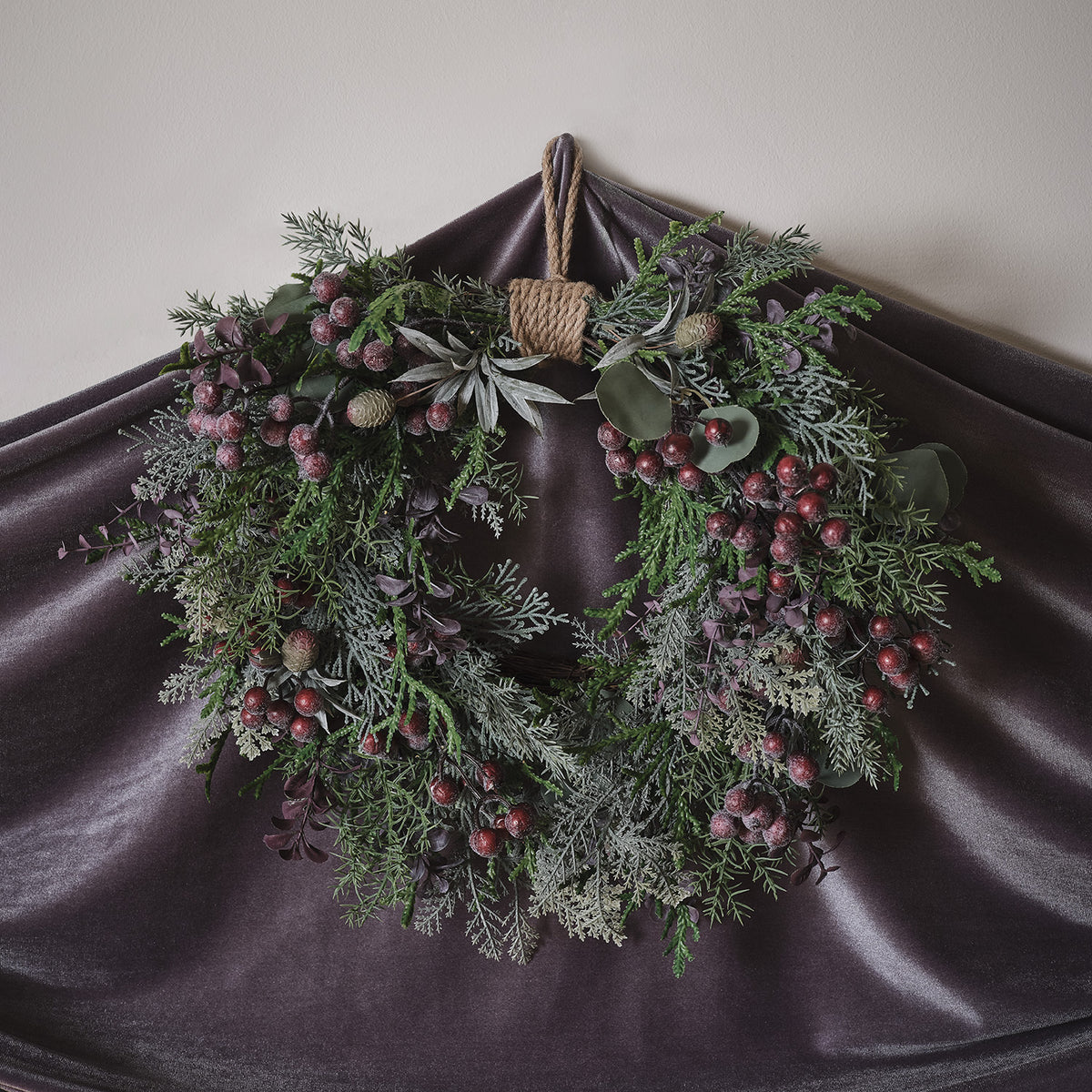 Nahaufnahme des Weihnachtskranzes mit lila Beeren, grünen Zweigen und warmweißen LED-Lichtern
