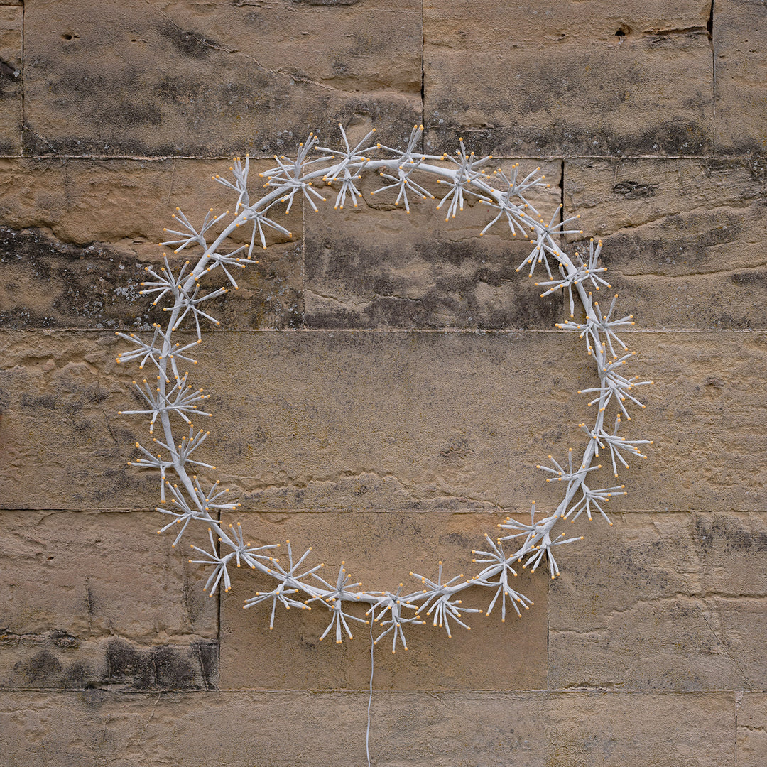 Weihnachtskranz mit weißen sternförmigen LED-Clustern an einer Steinwand