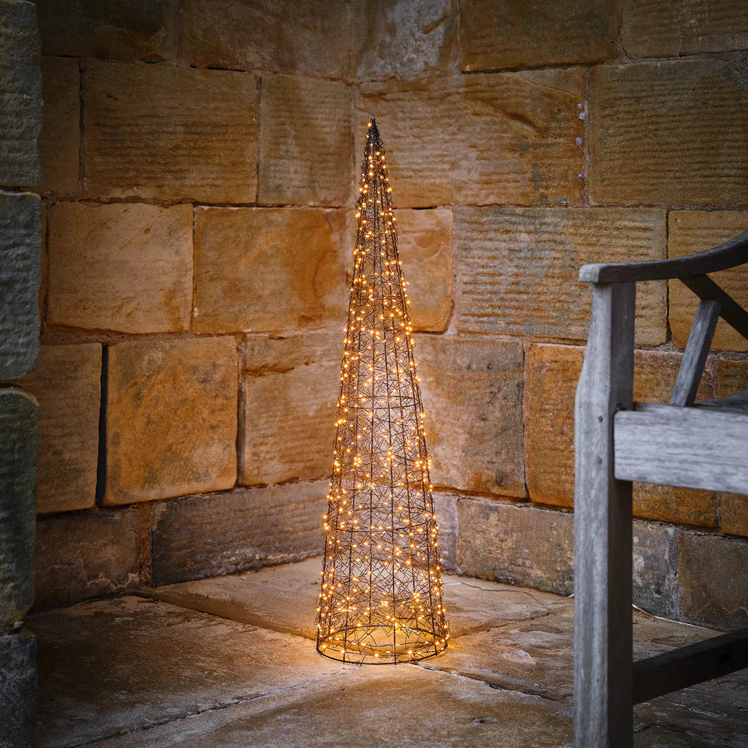 Leuchtpyramide aus Draht mit warmweißen LEDs vor rustikaler Steinwand neben Holzstuhl