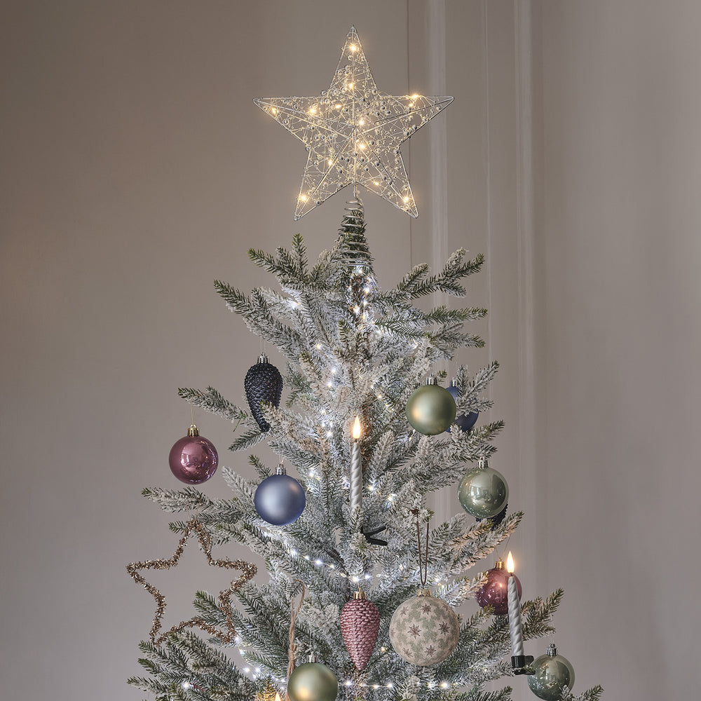 Weihnachtsbaum mit LED-Sternspitze und buntem Baumschmuck in einem Wohnzimmer