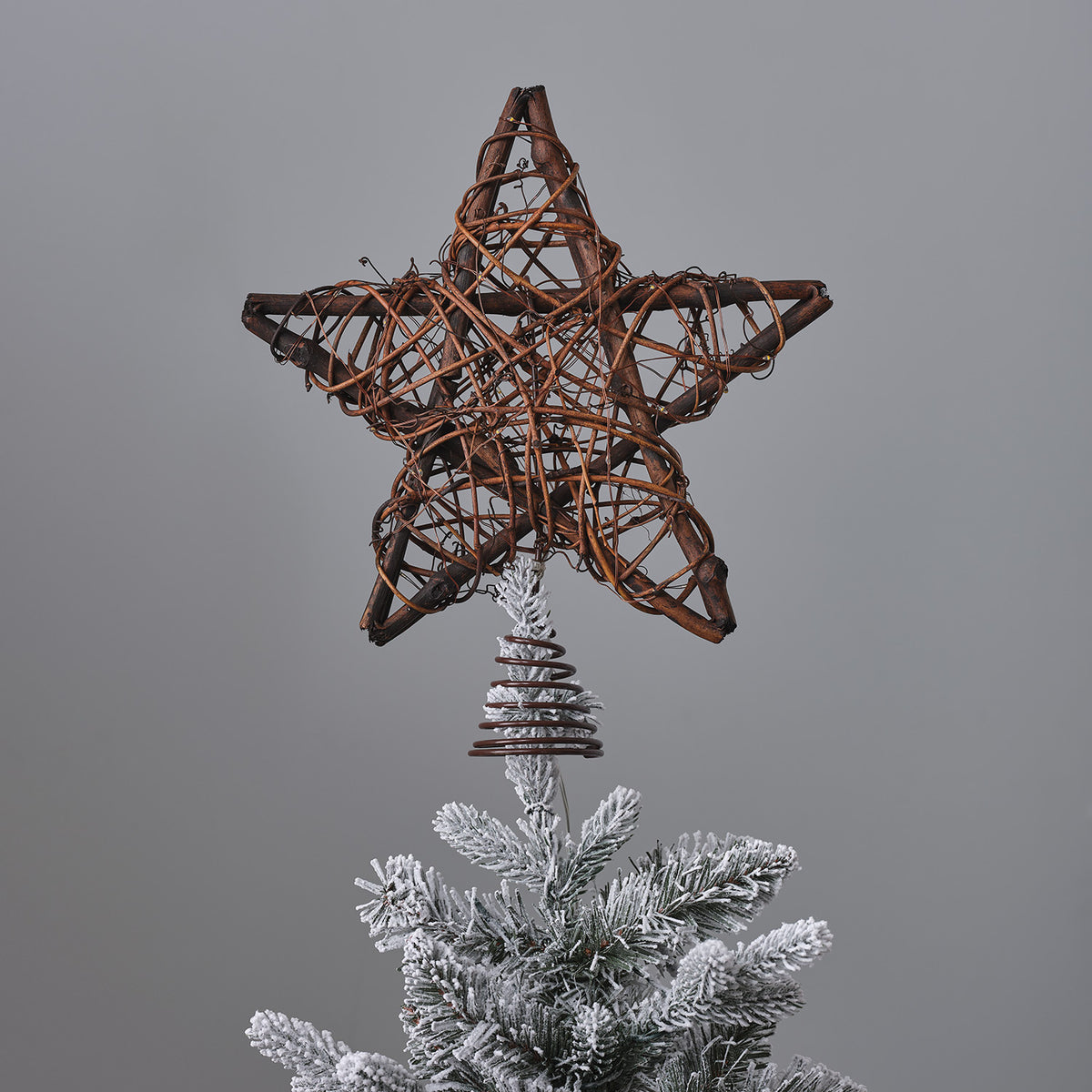 Unbeleuchteter Weihnachtsbaumstern aus Holz und Rattan mit Metallspirale auf schneebedeckter Tannenspitze