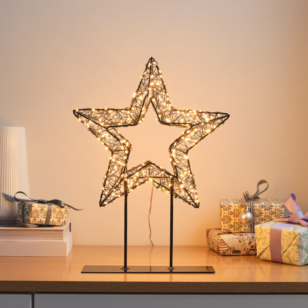 LED-Stern aus Draht mit 300 warmweißen Micro-LEDs auf Metallbasis, dekoriert mit Geschenken im Hintergrund