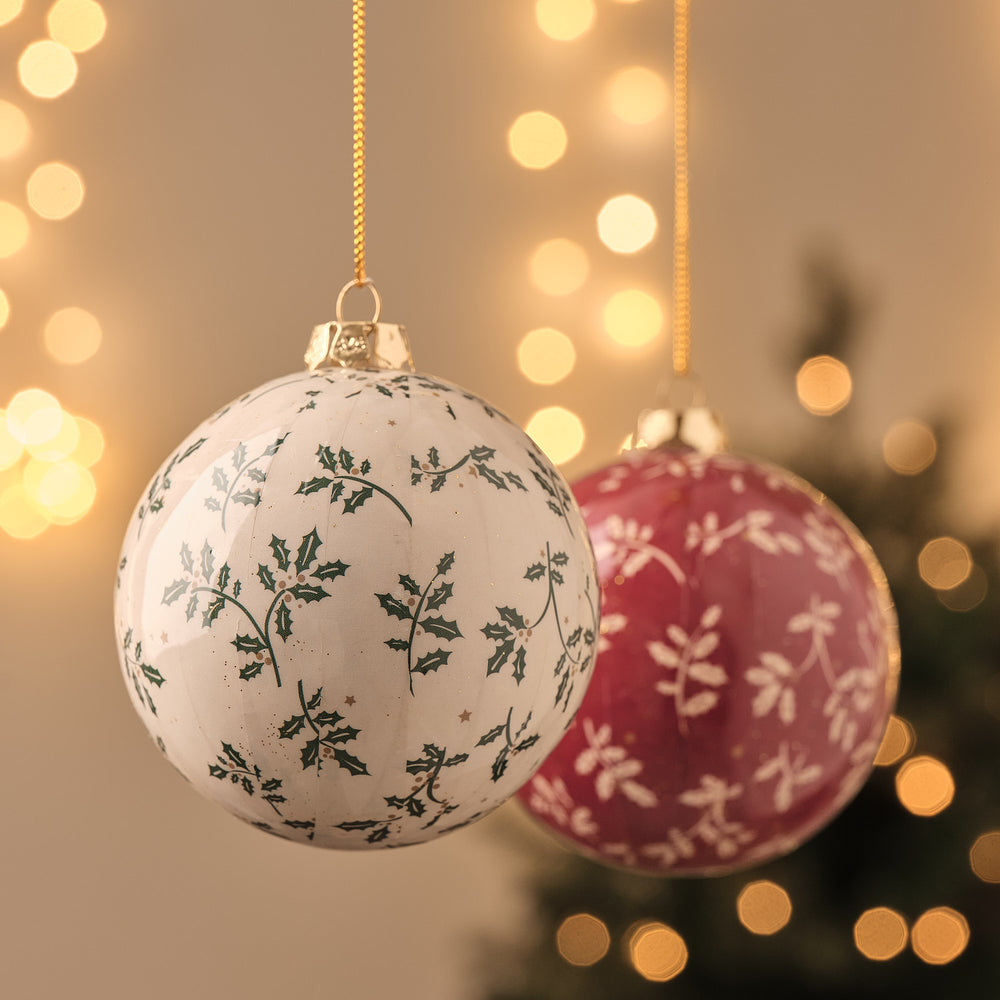 Weihnachtskugeln in Creme und Bordeaux mit floralem Blattmuster, hängend vor funkelndem Lichterglanz.