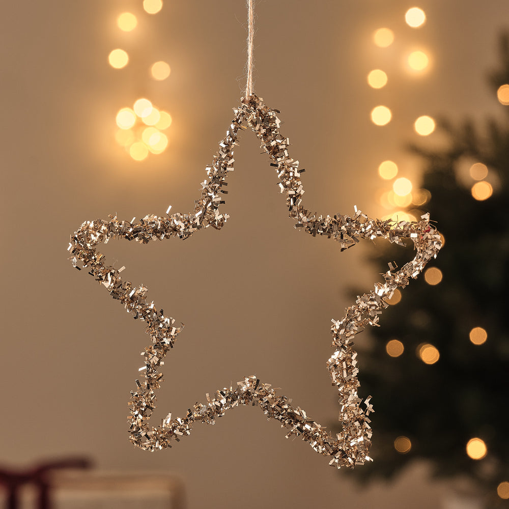 Sternförmiger Drahtstern-Anhänger mit Glitzerbesatz, hängend vor beleuchtetem Tannenbaum.