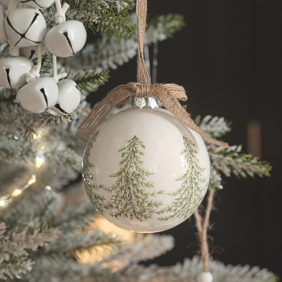 Weiße Weihnachtskugel mit Tannenzweig-Motiv und Jute-Schleife an bereiftem Tannenzweig.