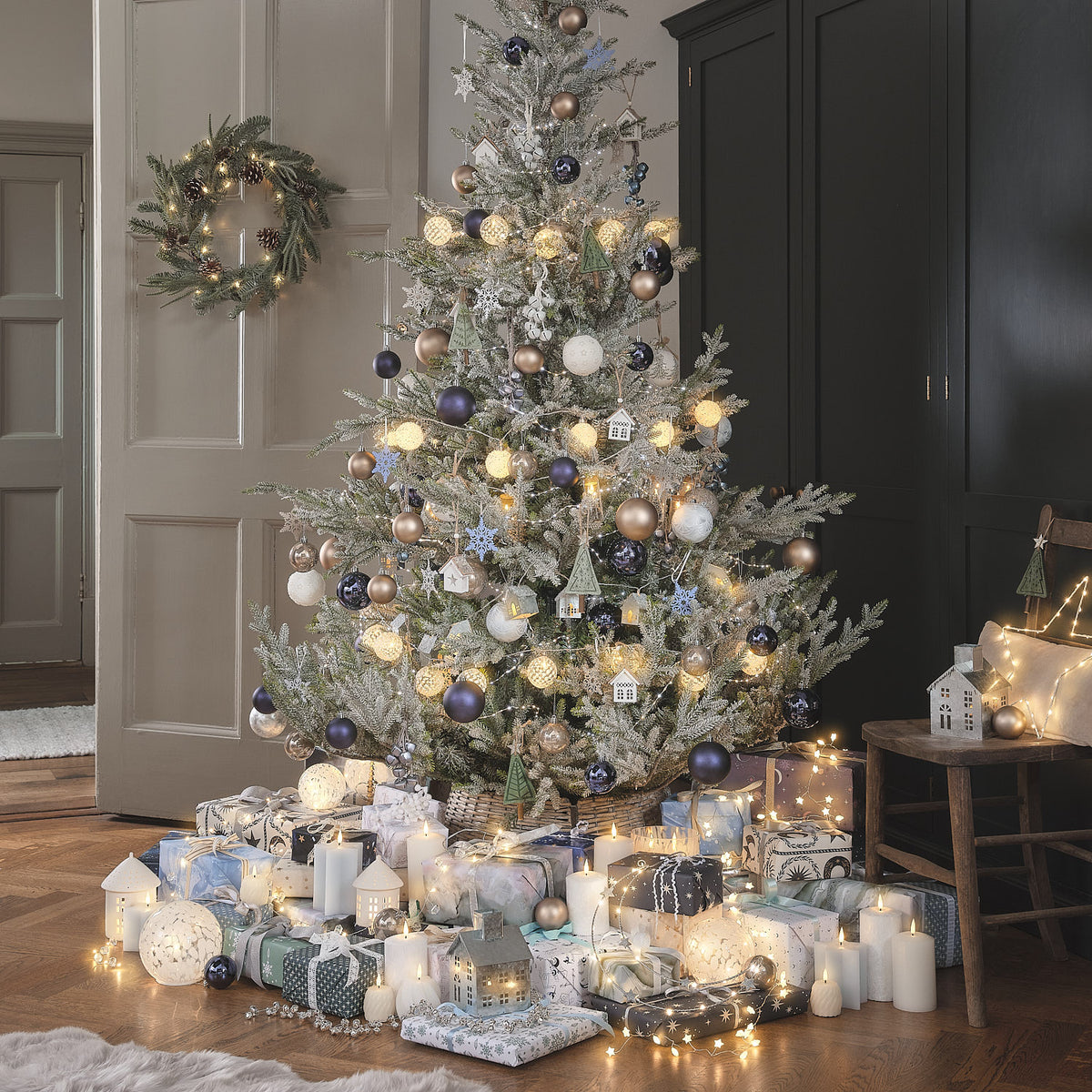 Weihnachtlich dekoriertes Wohnzimmer mit beleuchtetem Baum und Kranz an der Tür.