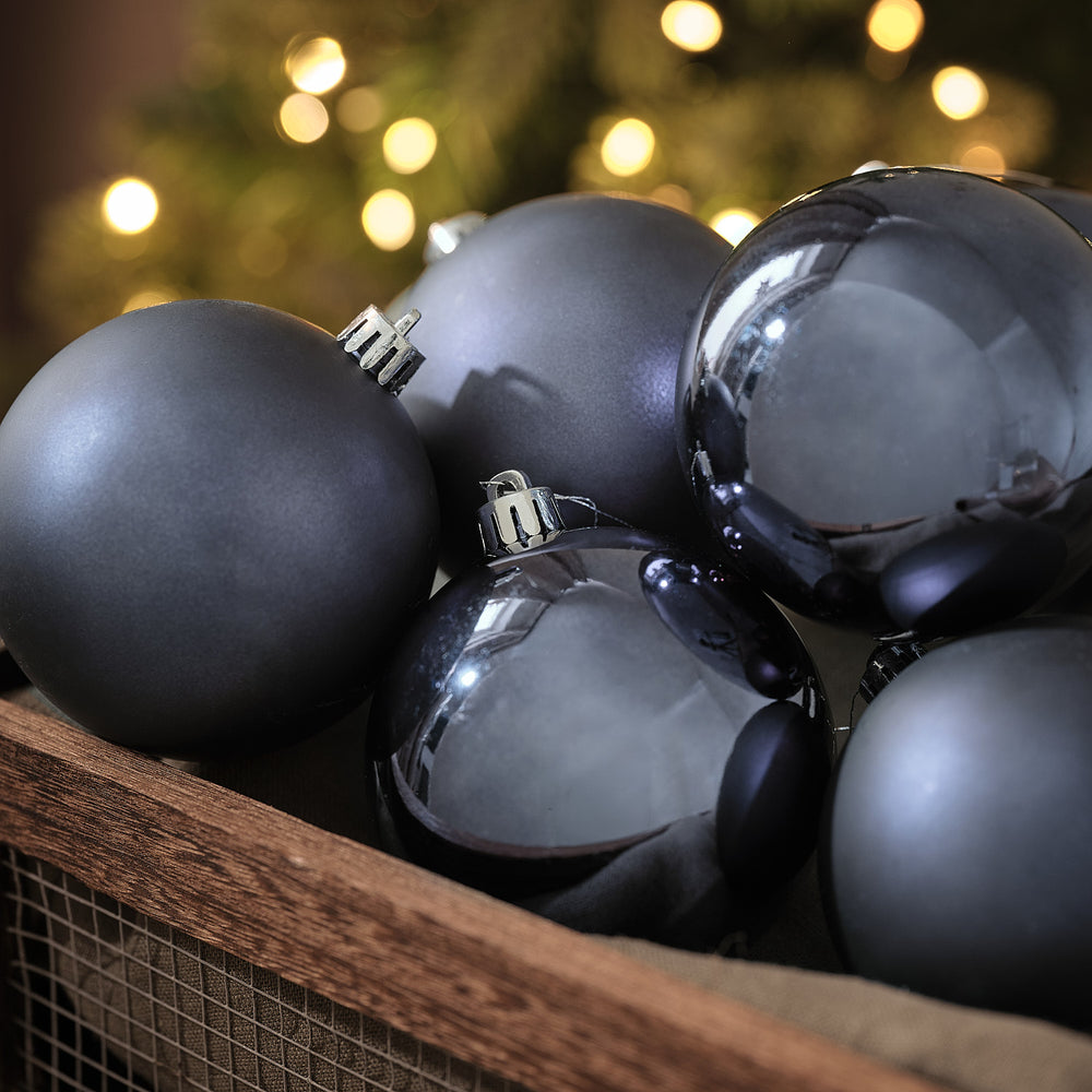 Blaugraue Weihnachtskugeln in matter und glänzender Optik in Holzkiste vor Lichterglanz.