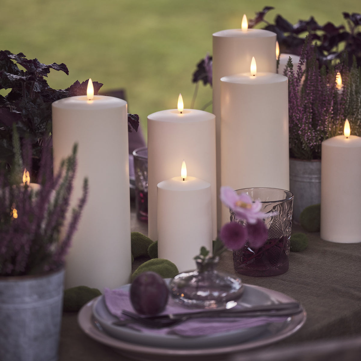 LED-Kerzen mit violetten Pflanzen und gedecktem Tisch mit Obst und Besteck