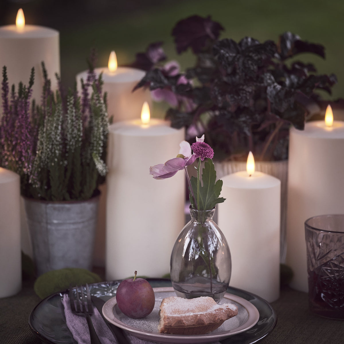 LED-Kerzen auf Tisch mit Teller, Glas und violetten Pflanzen dekoriert