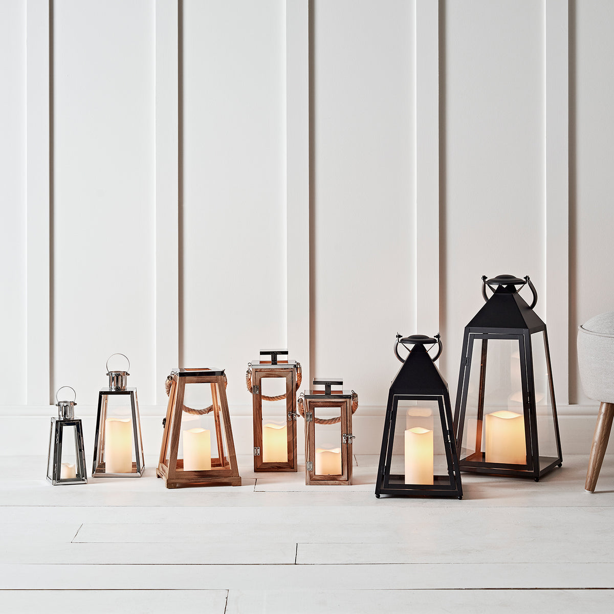 Reihe verschiedener LED Laternen aus Edelstahl, Holz und Schwarz vor weißer Wand