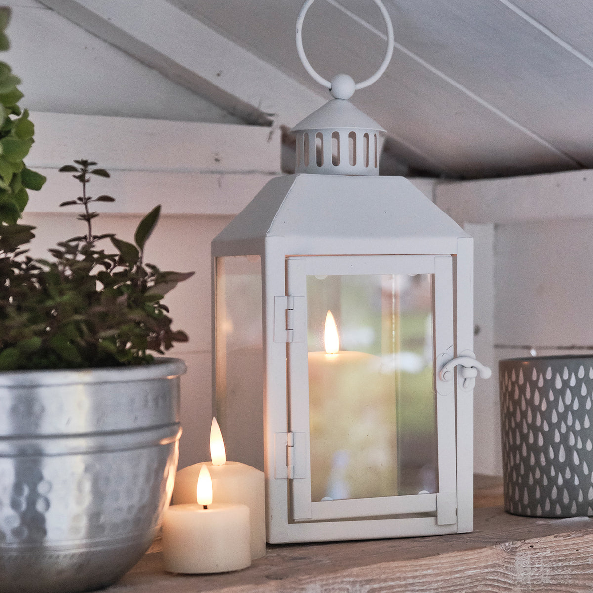 Nahaufnahme weiße Laterne mit TruGlow LED-Kerze neben Metalltopf und weiteren Kerzen