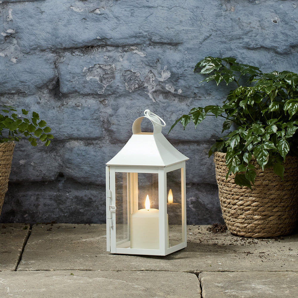 Weiße Gartenlaterne mit TruGlow LED-Kerze auf Steinboden neben Pflanzen