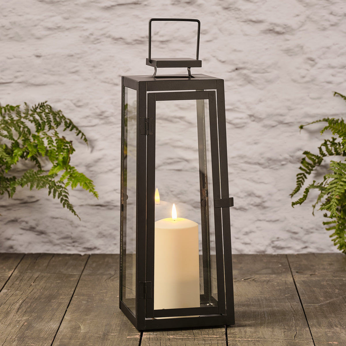 Große schwarze Metalllaterne mit Glas und TruGlow LED-Kerze auf Holzboden vor weißer Wand