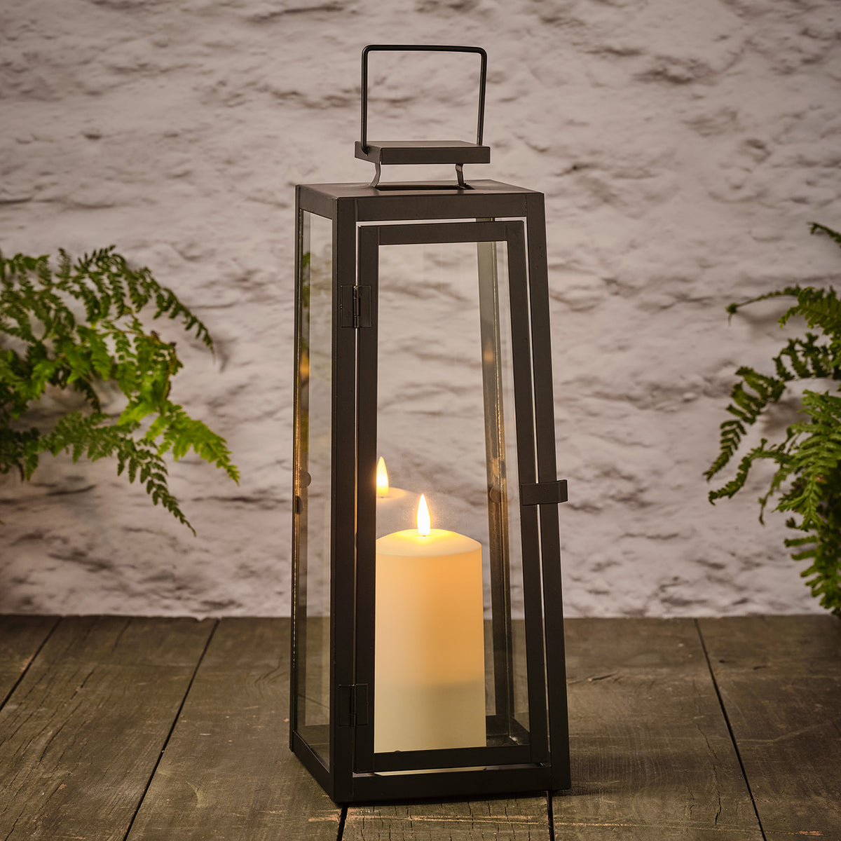 Große schwarze Laterne mit Glas und flackernder TruGlow LED-Kerze auf Holz vor weißer Wand