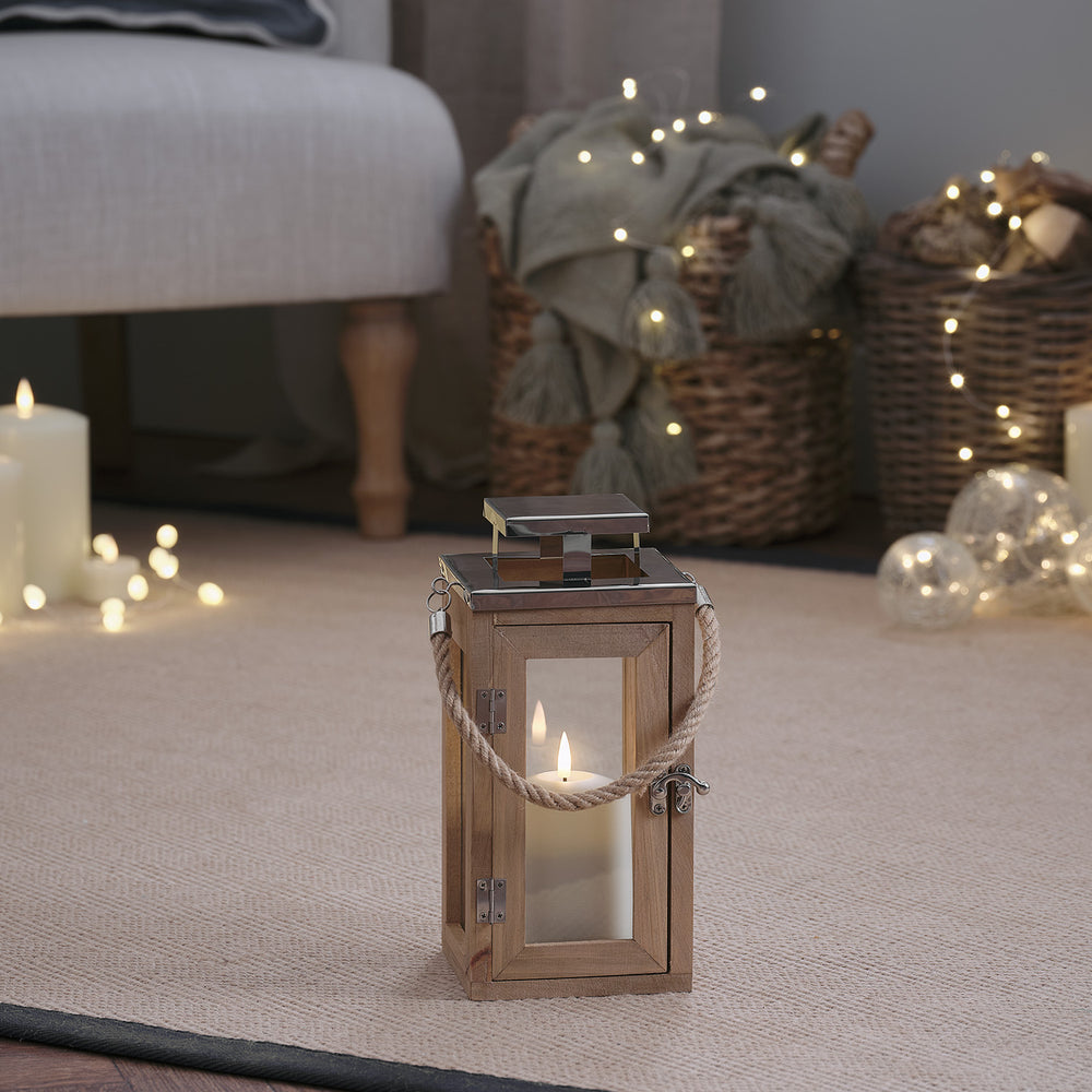 Kleine Holzlaterne mit LED-Kerze auf Teppich vor Korb und Lichterkette im Wohnzimmer