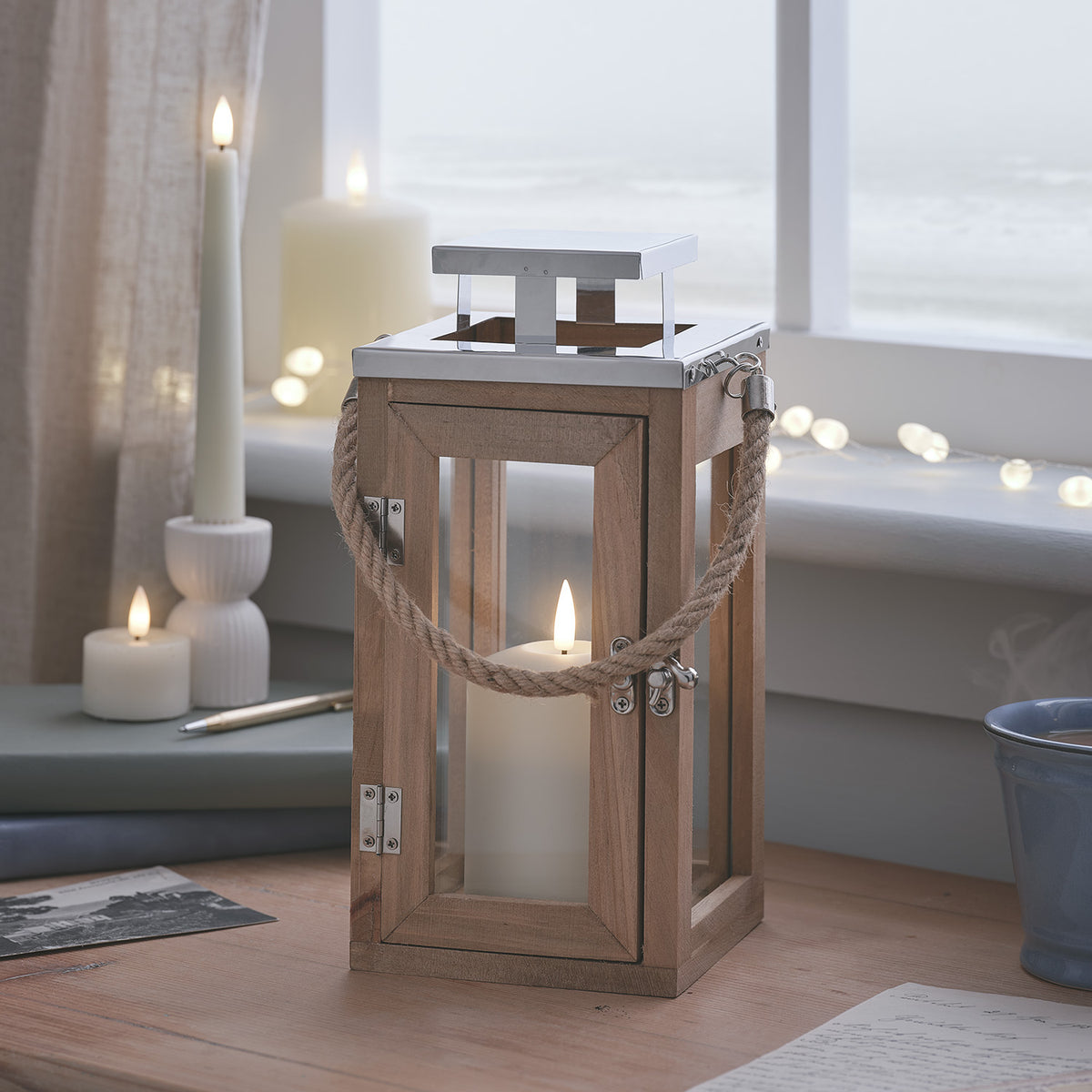 Holzlaterne mit TruGlow LED-Kerze auf Holztisch vor Fenster mit Meeresblick